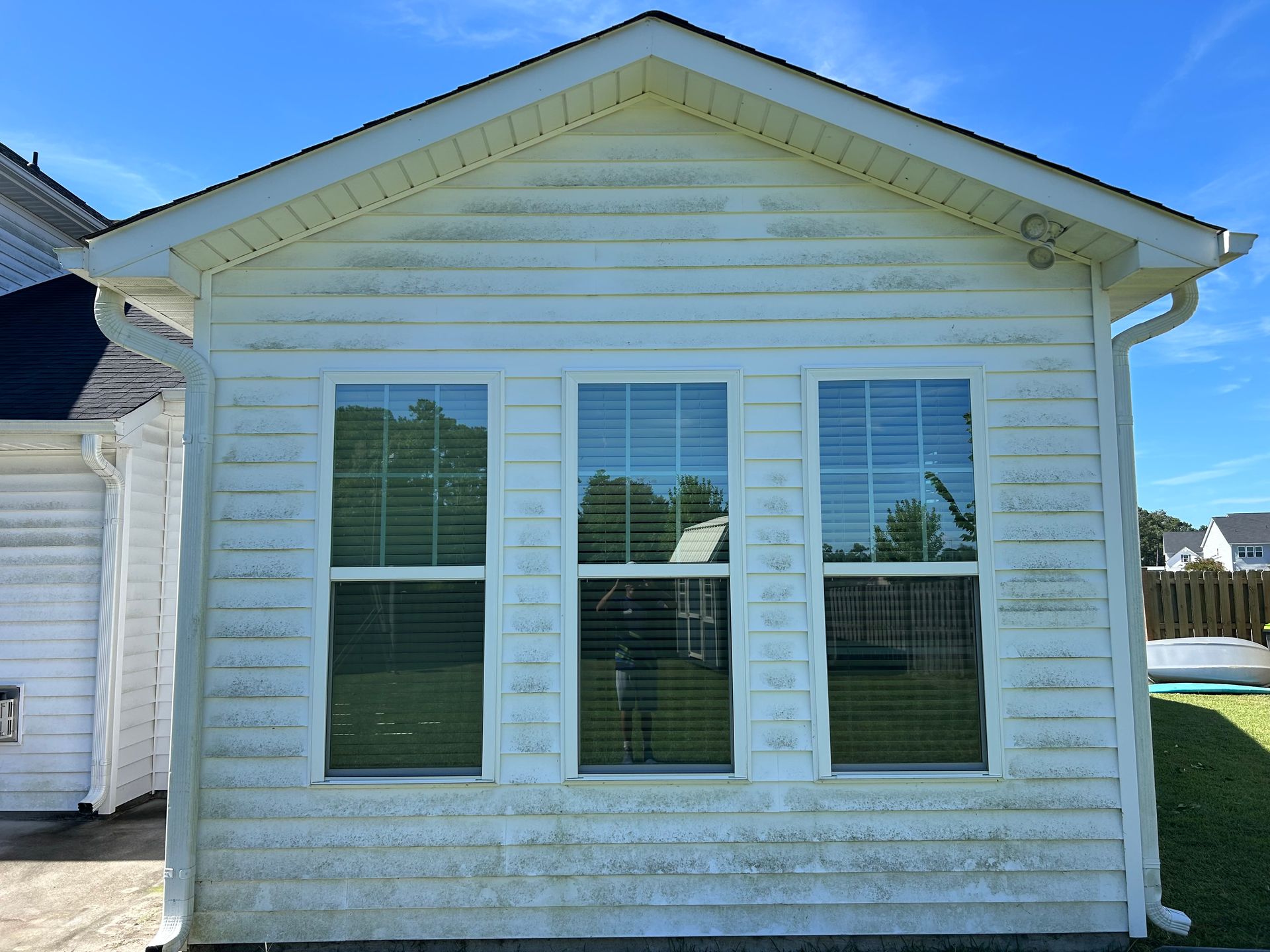 White siding with three windows, showing greenish discoloration.