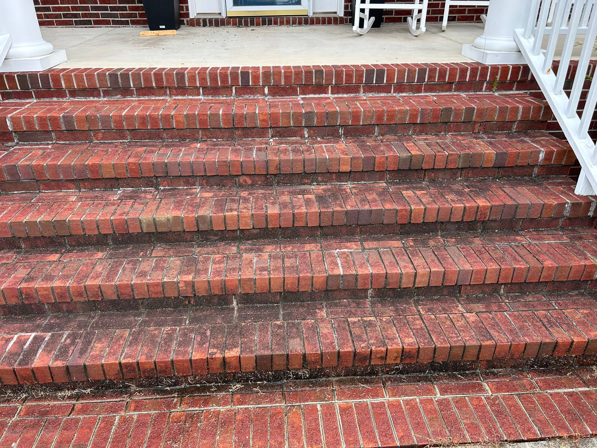 Brick steps leading up to a porch, with white railing on the right. The brick is red-orange and has some dark areas.