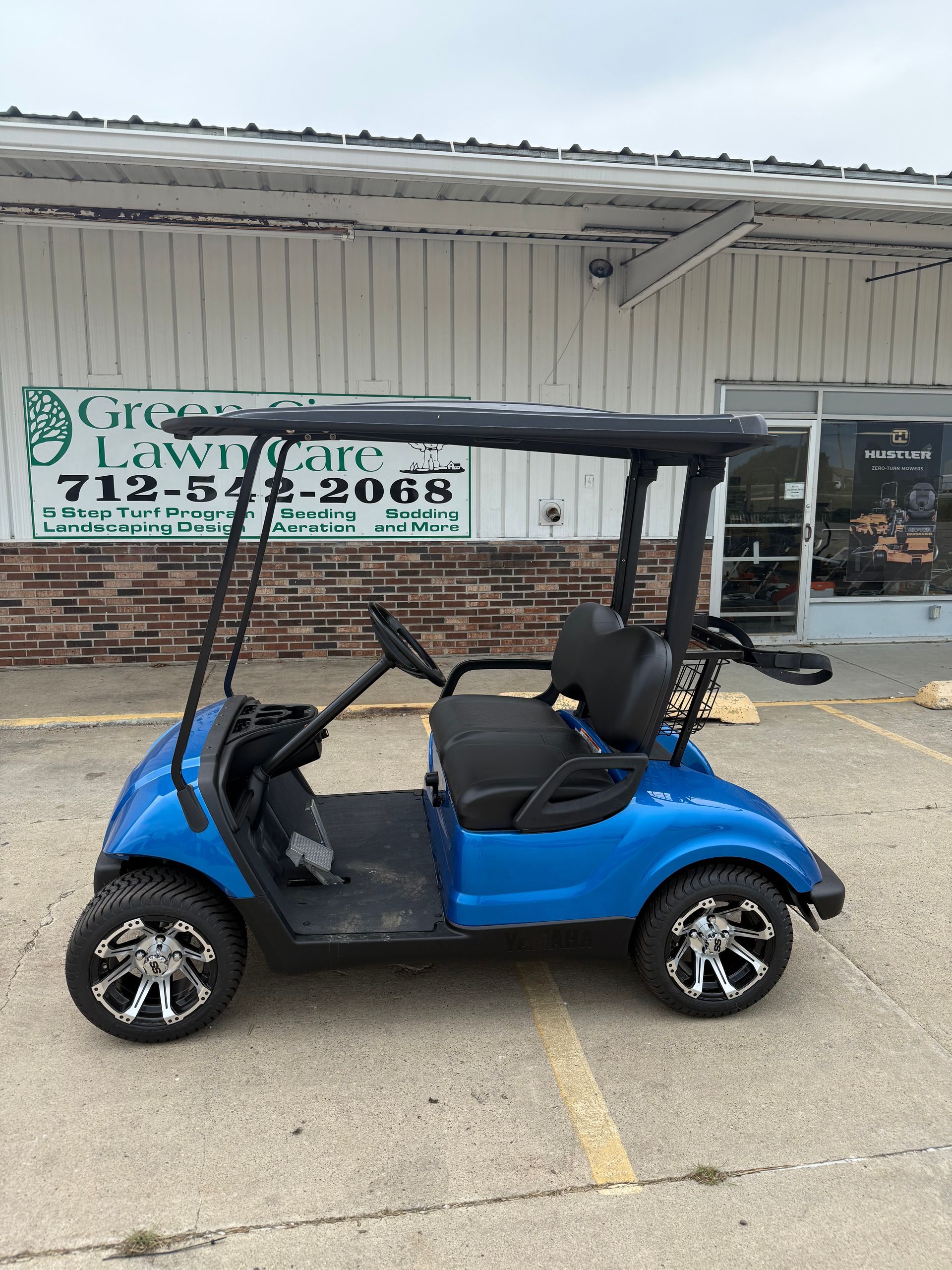 Dark gray golf cart parked on a sunny lot. It has a black roof and seats, with black and silver wheels.