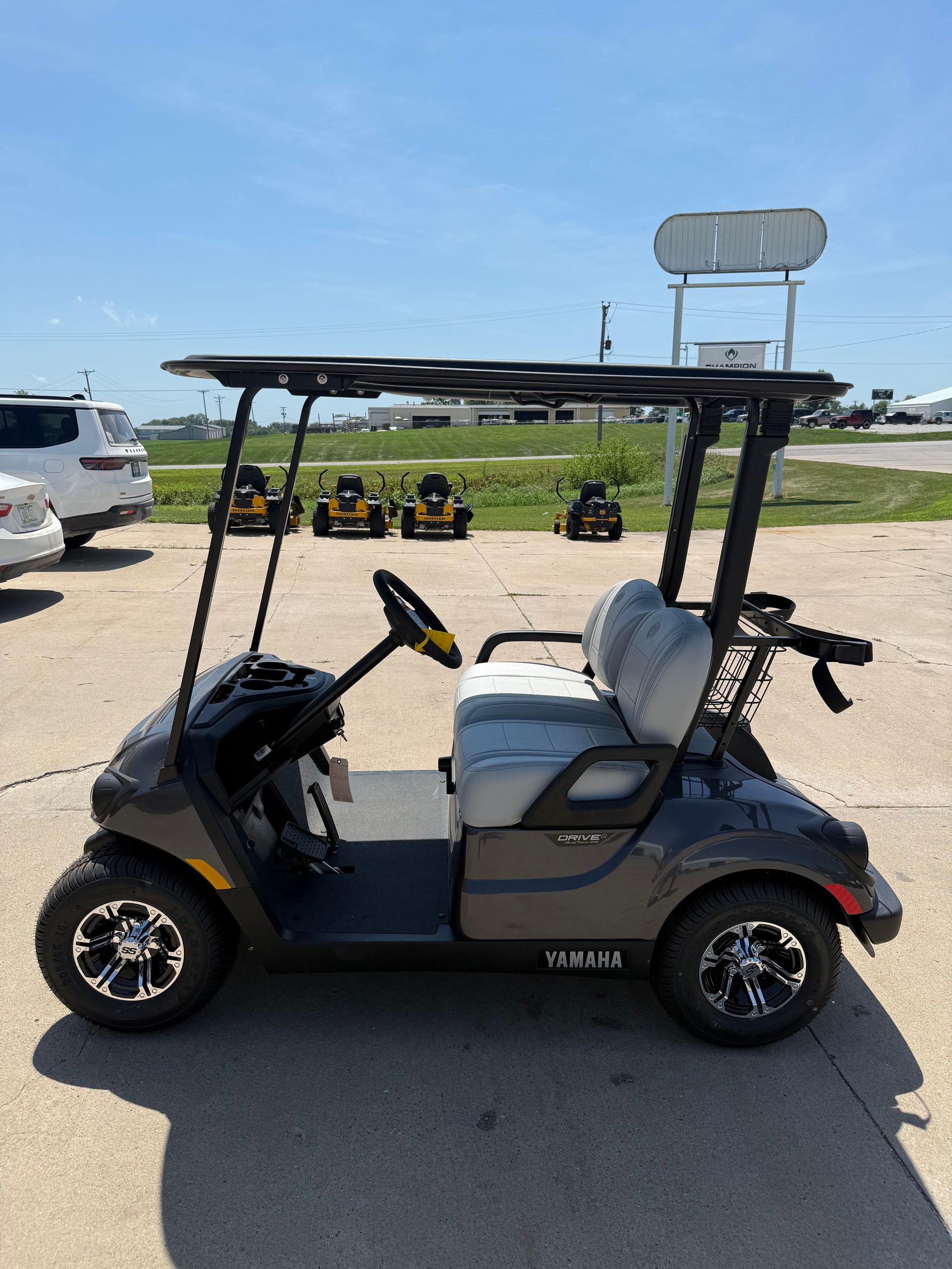 Dark gray golf cart parked on a sunny lot. It has a black roof and seats, with black and silver wheels.