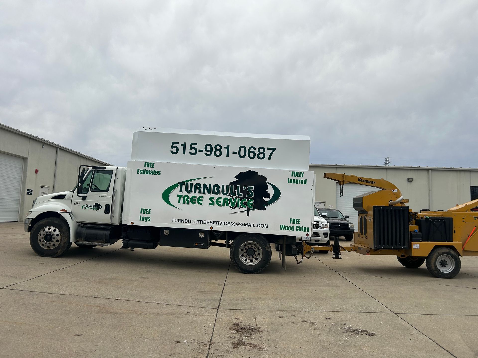 White tree service truck with wood chipper trailer in front of a building.