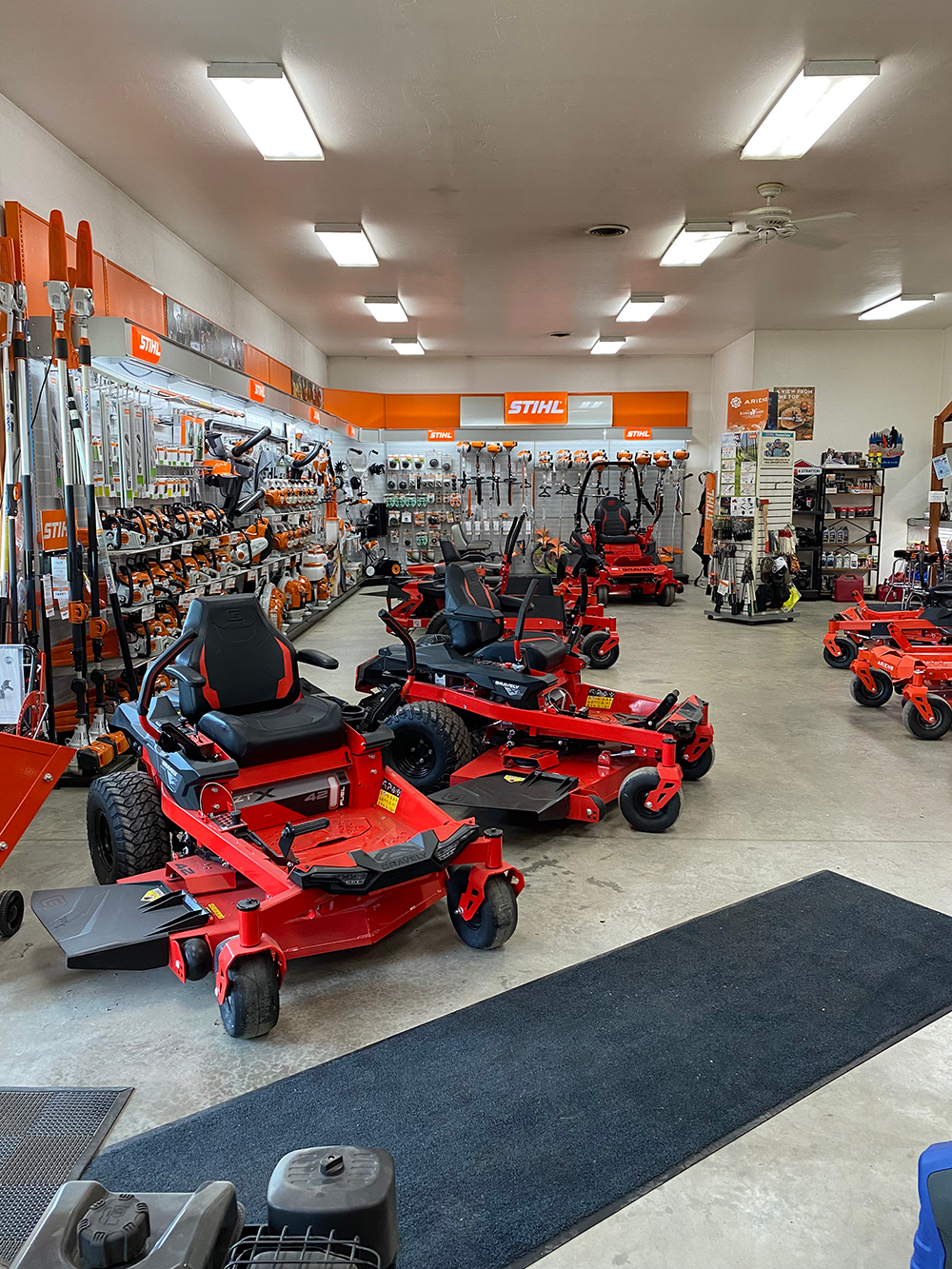 The interior of a Stihl equipment store featuring several red zero-turn lawn mowers displayed on a concrete floor.