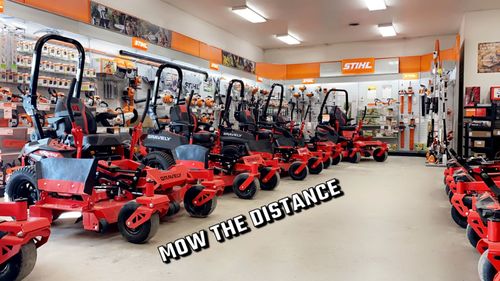 A row of red STIHL zero-turn lawn mowers on display inside a dealership, with the slogan 