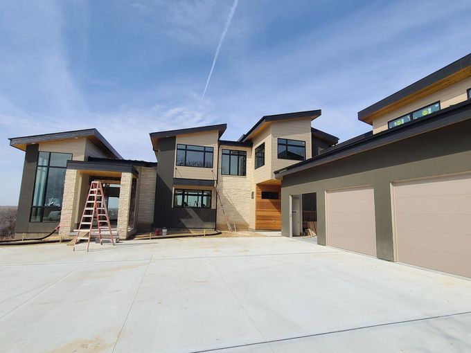 Modern house exterior with stone facade, large garage doors, and a wide driveway under a blue sky