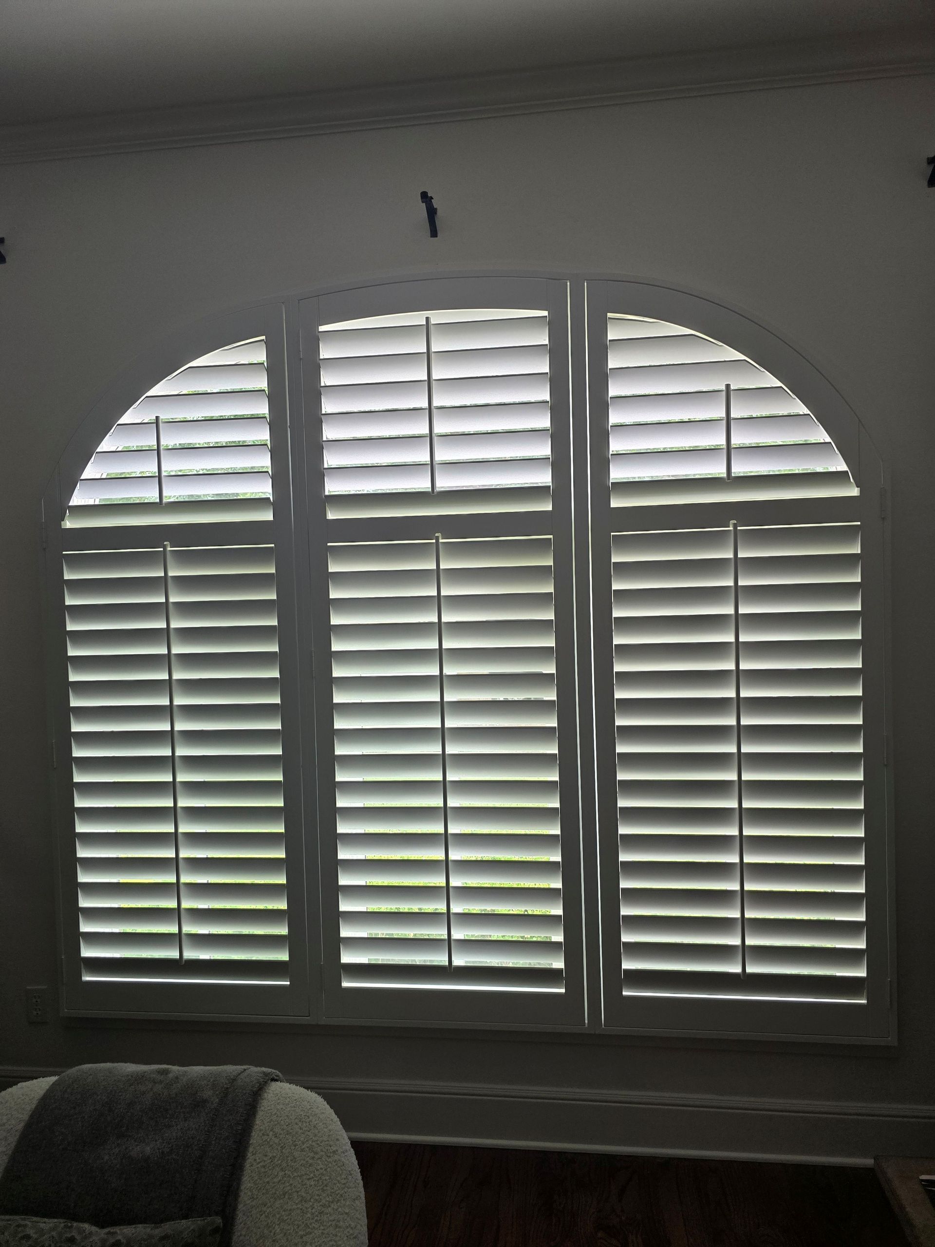 Arched window with white shutters, partially closed, indoors.  Sunlight streams through slats.