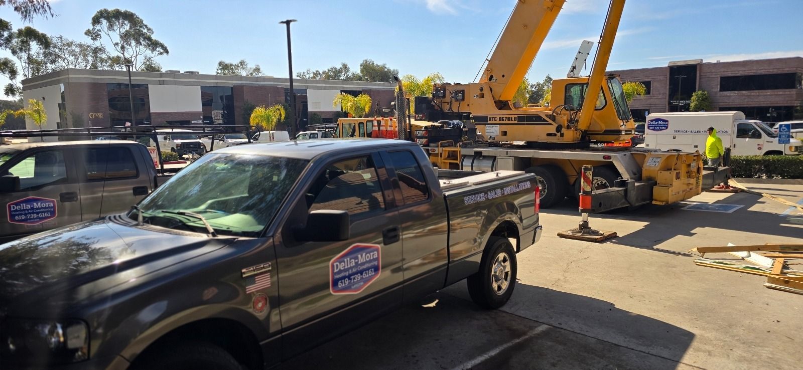 Construction site with crane, trucks, and building. Gray truck in foreground. Yellow crane arm extended.
