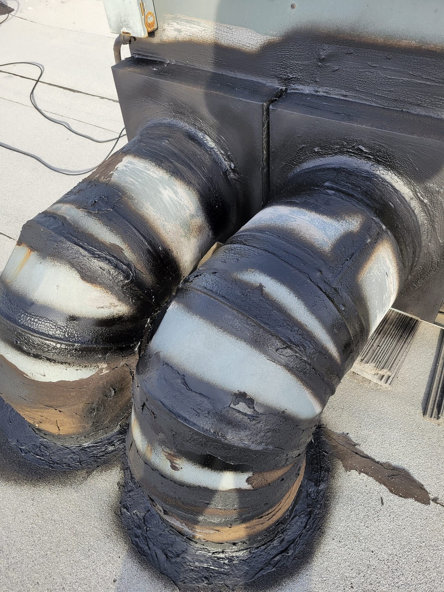 Black tar sealant around metal HVAC ductwork elbows on a rooftop.