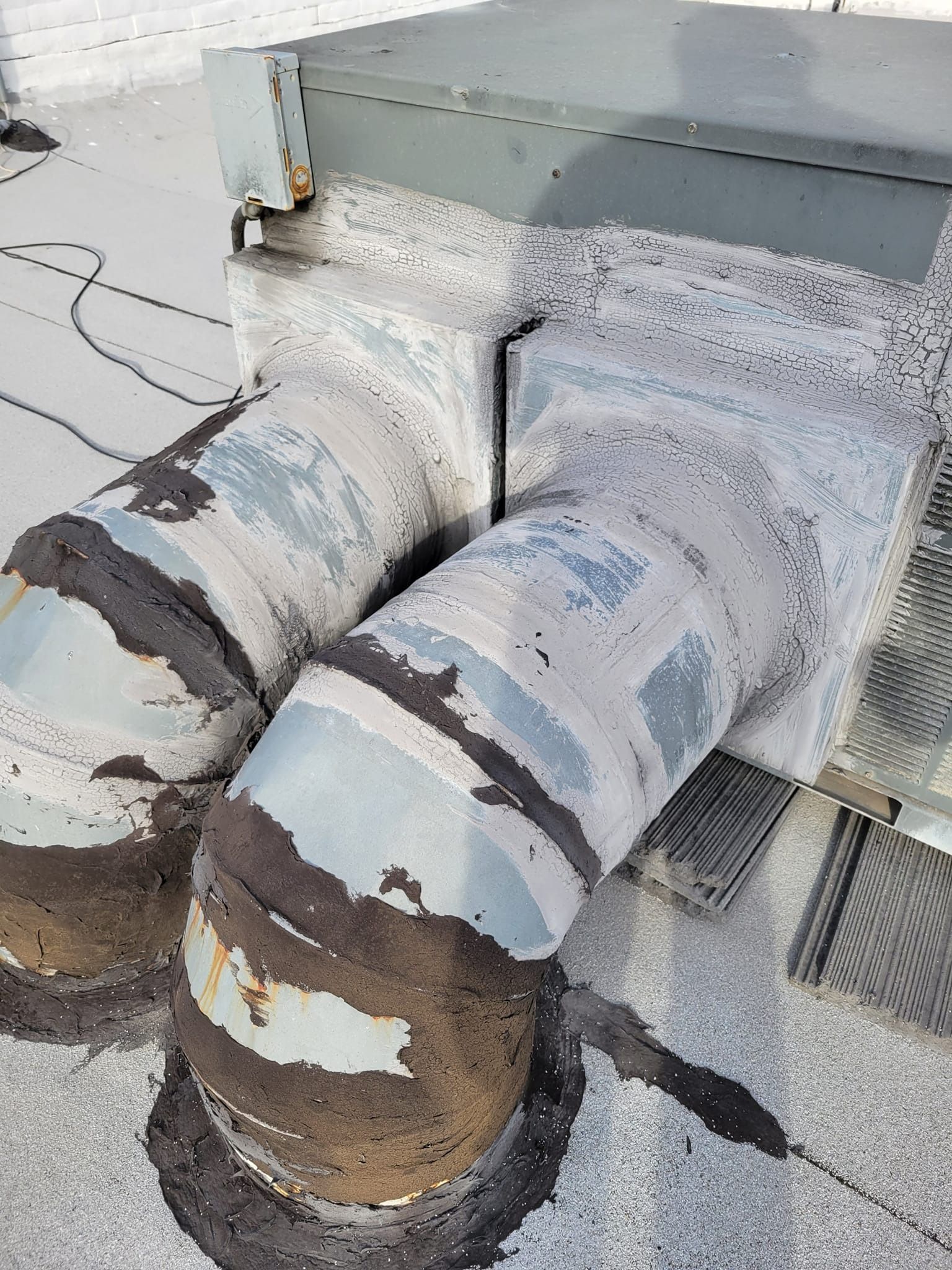 Two metal ventilation ducts on a flat rooftop, sealed with dark sealant.