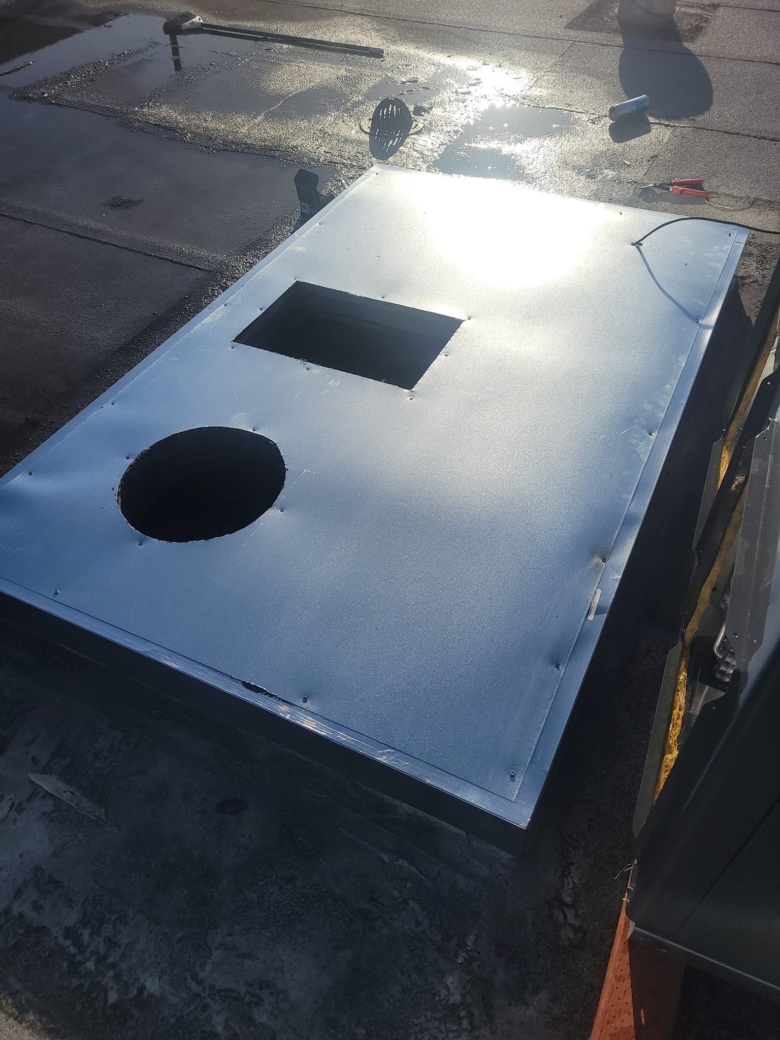 New roofing material patch on a dark rooftop. Rectangular with a square and a circular cutout.