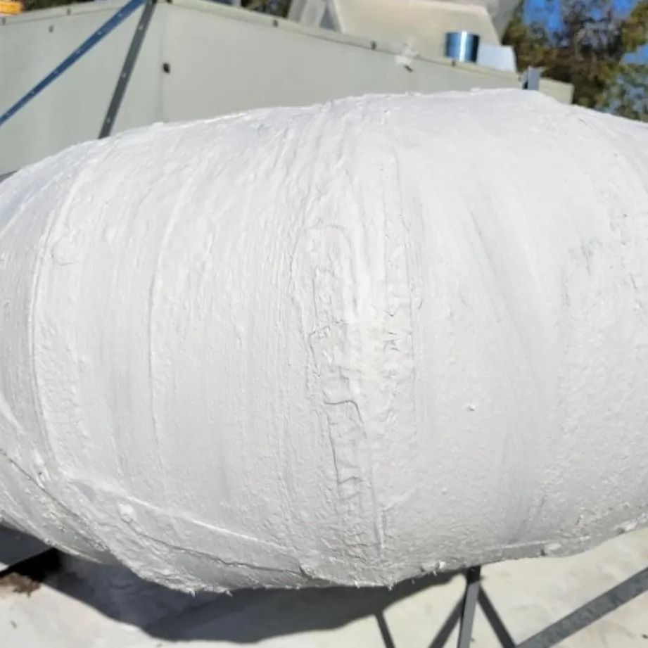 White painted object, cylindrical in shape, on a rooftop with mechanical equipment in the background.