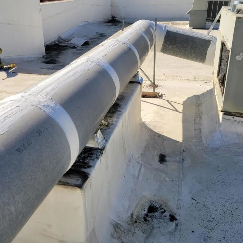 Rooftop view of a large insulated pipe, secured with white tape, running over a white painted surface.