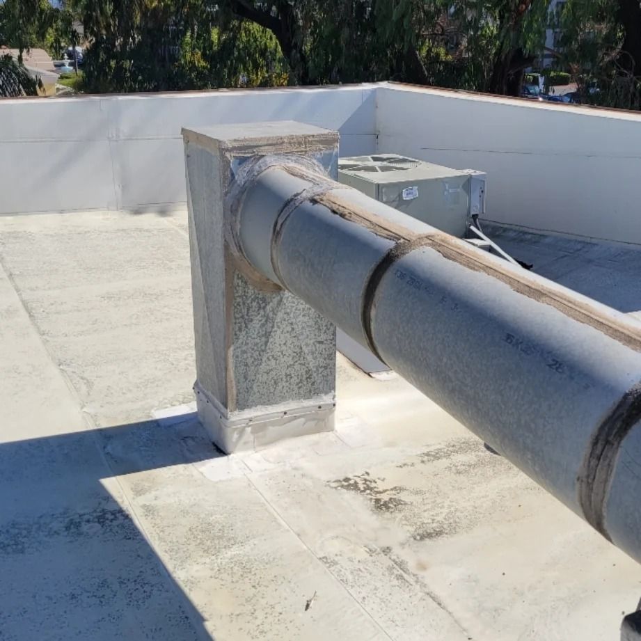 Metal pipe extending from a square pillar on a flat rooftop with an HVAC unit visible.