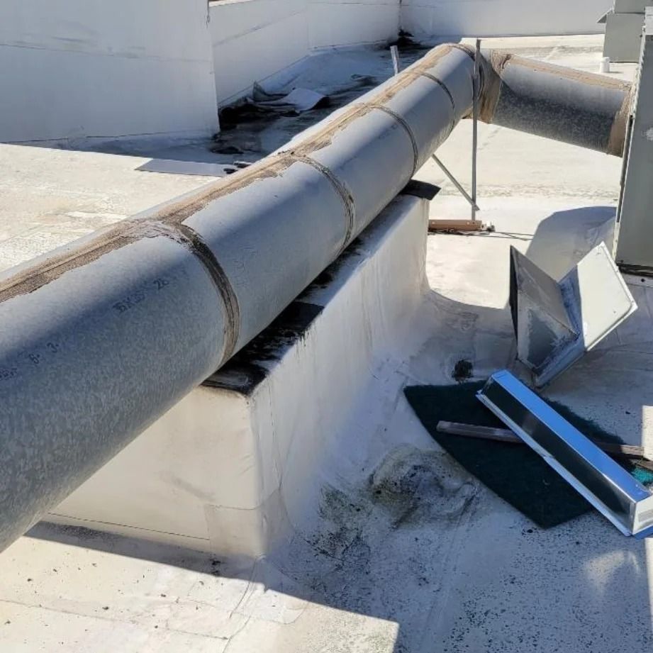 Rooftop with large metal pipes, some damage to the flat surface, and an HVAC unit.