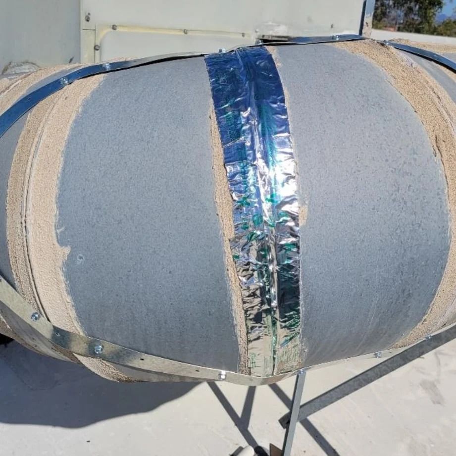 Large, round, insulated duct on a rooftop, with metal banding and silver tape.