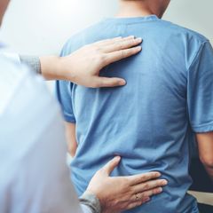 A man in a blue shirt is getting his back examined by a doctor.