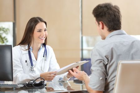 A doctor is talking to a patient at a desk in a hospital.