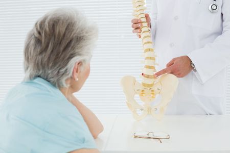 A doctor is showing an elderly woman a model of a spine.