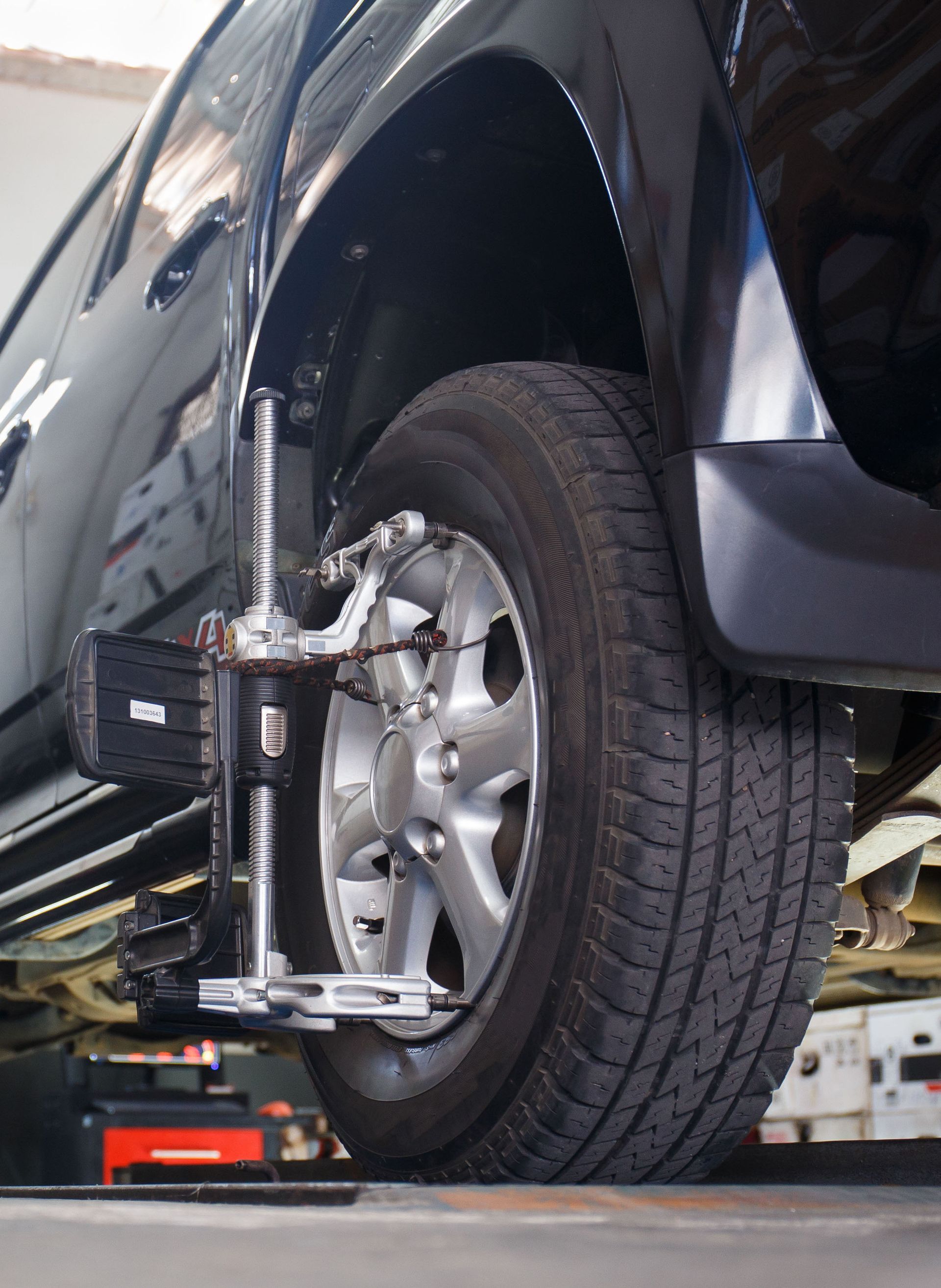 Black car tire with alignment equipment attached, in a repair shop.