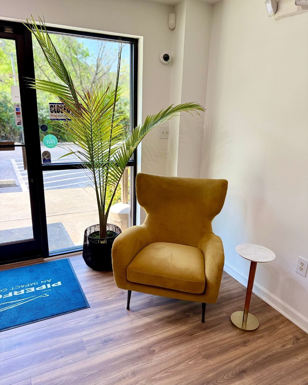Mustard yellow chair near a plant and table in an office lobby with wooden floors and a door.