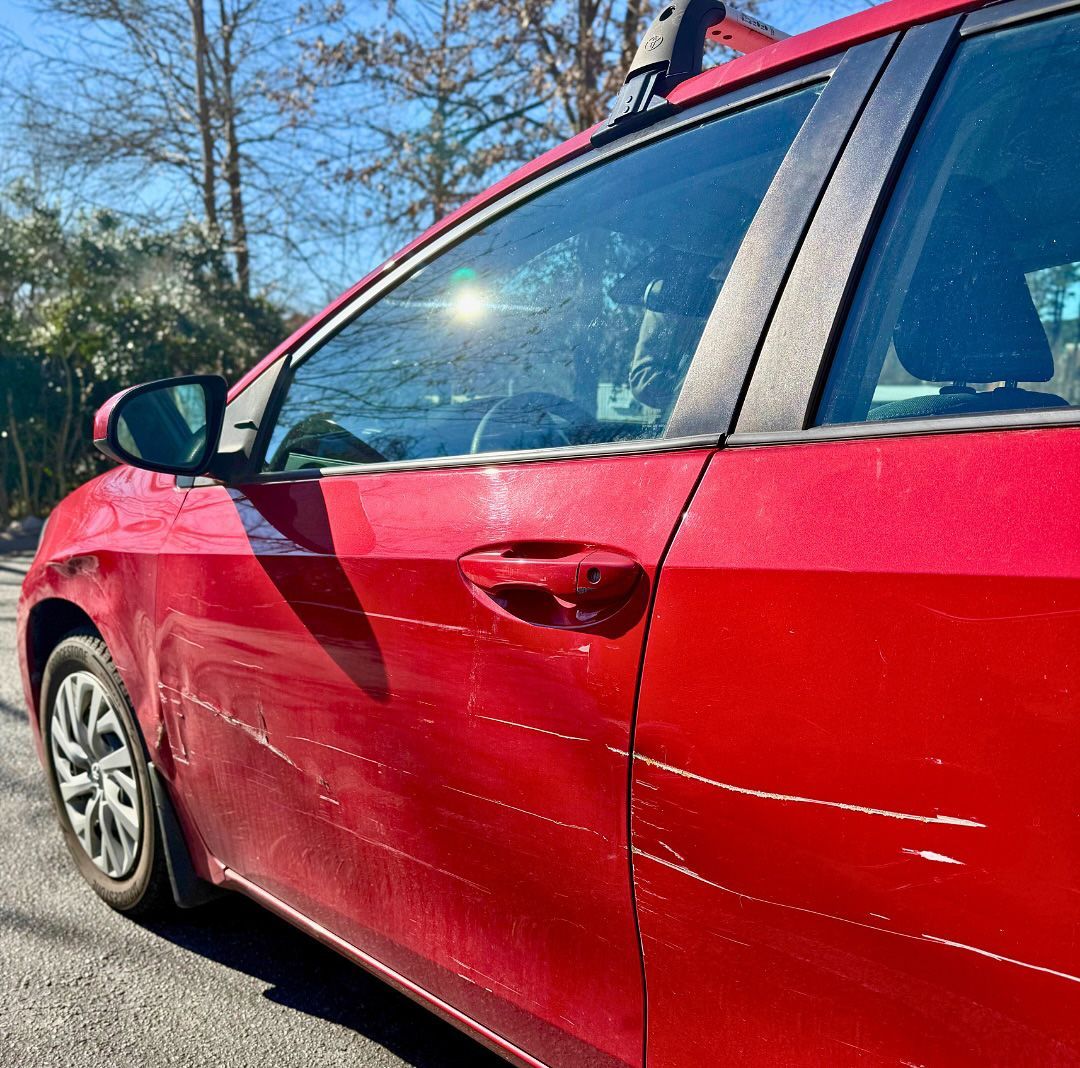 Red car parked outside on a sunny day; scratches visible on the door.