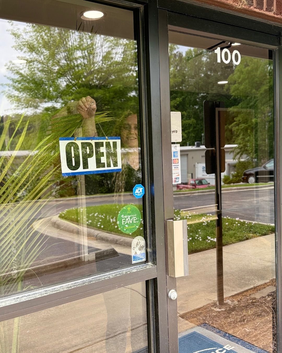 Open sign on a glass door with a person visible through the glass. Building number 100 visible.