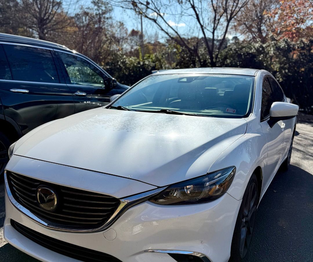 White Mazda 6 sedan parked outdoors next to a dark SUV on a sunny day.