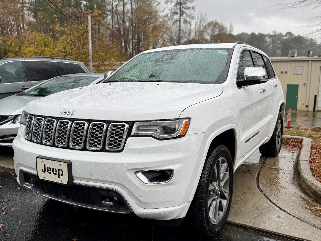 White Jeep Grand Cherokee parked on a wet day. Gray sky and a building in the background.