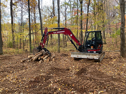 A red excavator is sitting in the middle of a forest next to a pile of logs.