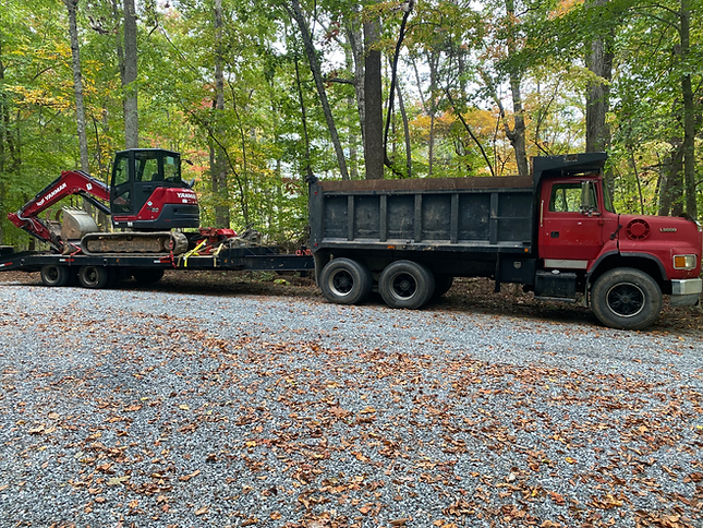 A dump truck is carrying an excavator on a trailer.