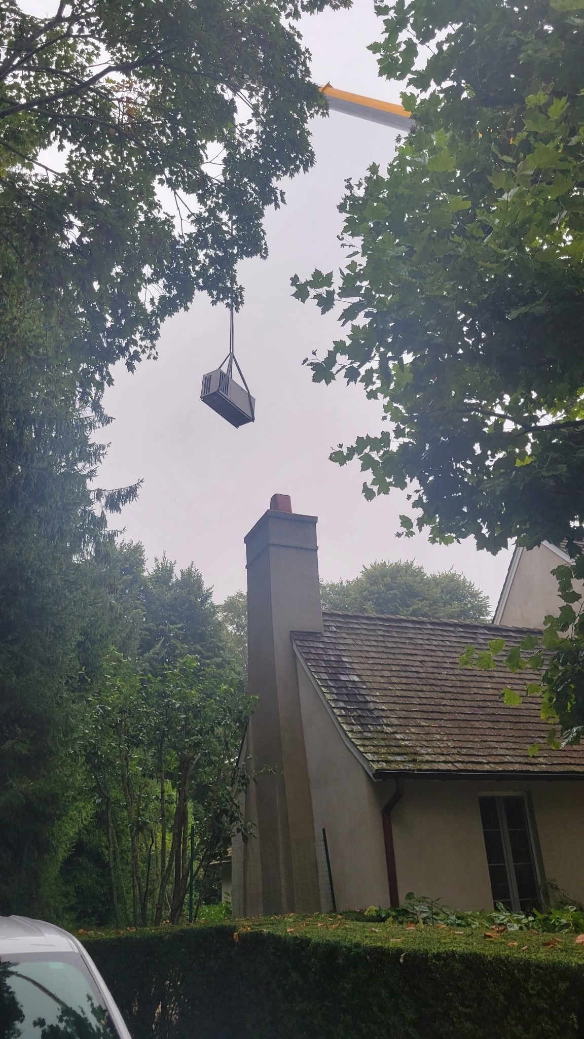 A car is hanging from a crane over a house