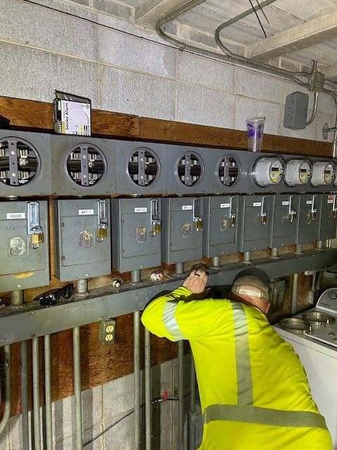 Electrician in yellow suit working on electrical meters in a utility room.