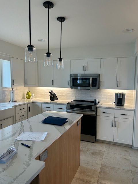 Modern white kitchen with island, countertops, and pendant lights. Stainless steel appliances and light wood accents.