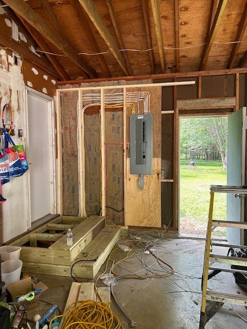 Garage under renovation: unfinished walls, new electrical panel, and wooden steps are visible.