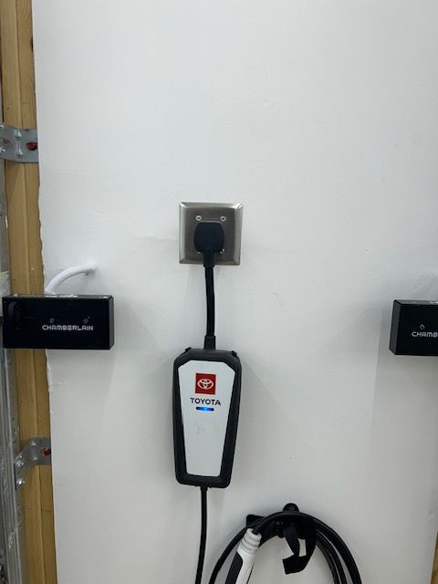 Wall with electric vehicle charger, outlet, and garage door openers.