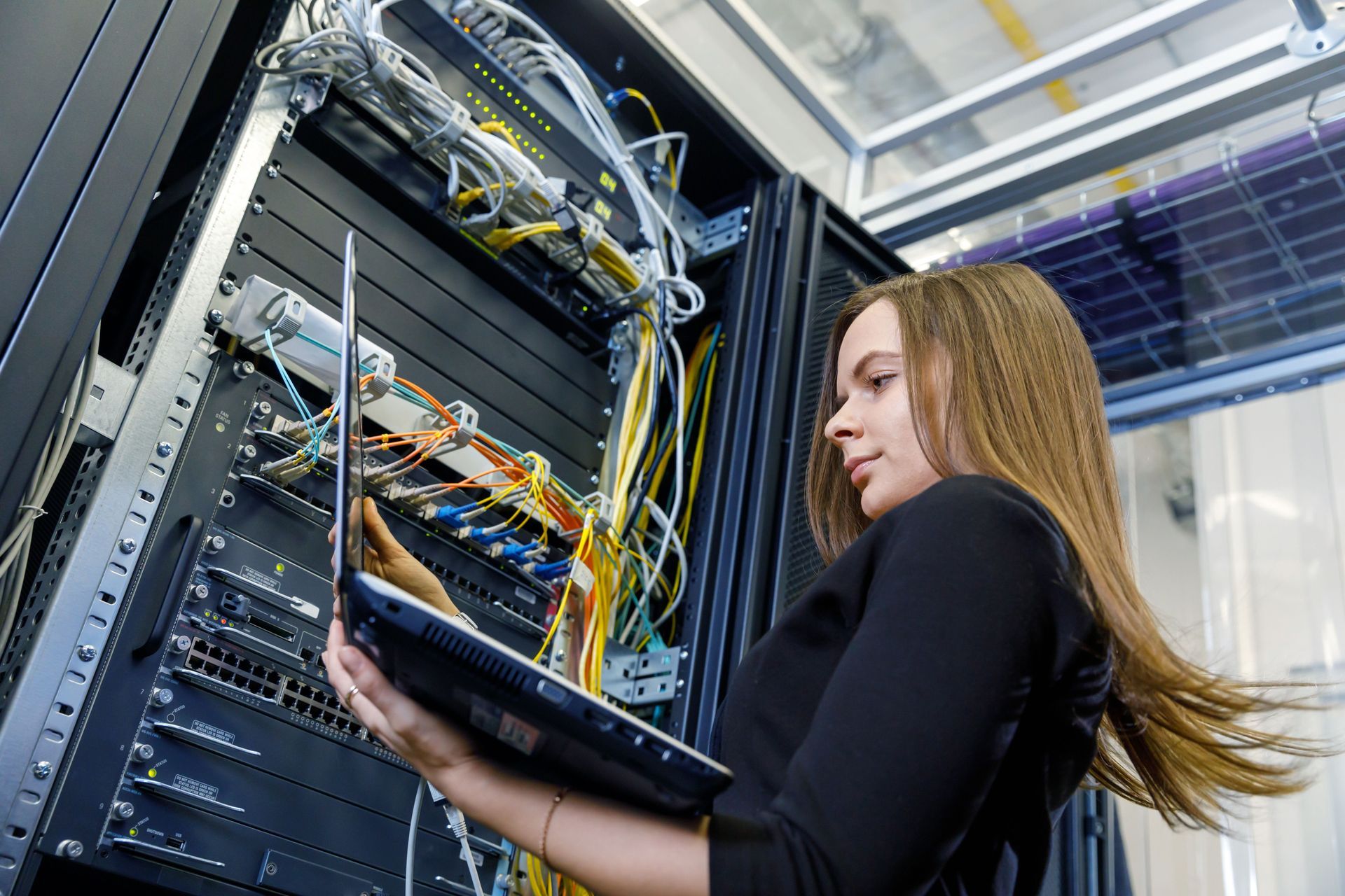 Woman with laptop troubleshooting server rack in data center.