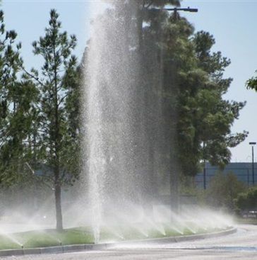 A fountain spraying water in a parking lot with trees in the background
