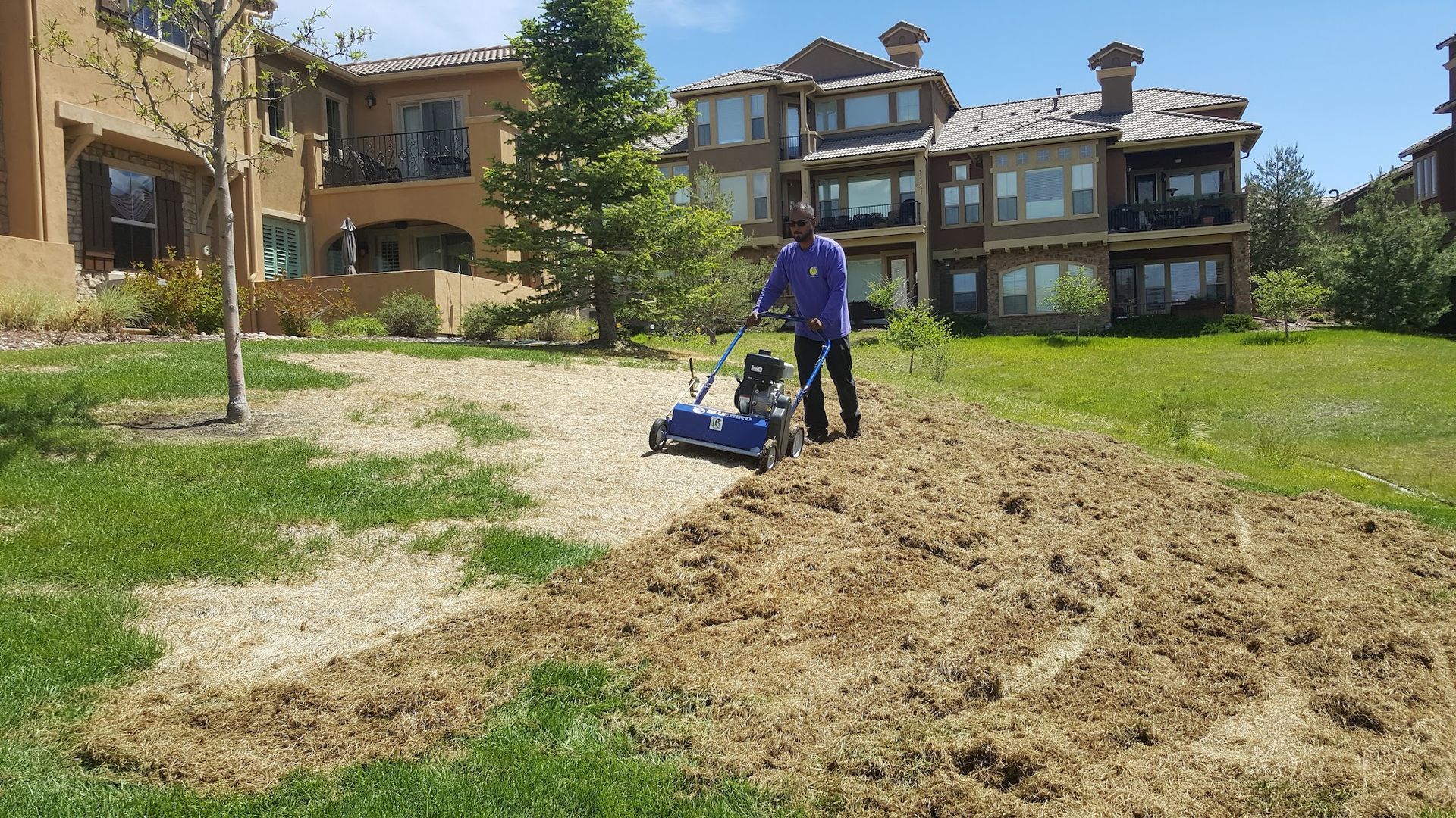 A man is plowing a lawn in front of a building.