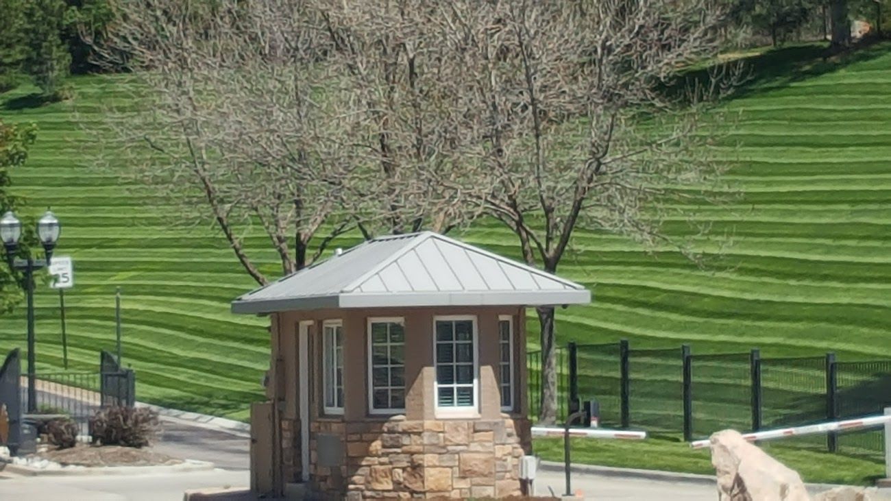 A small building with a metal roof is in the middle of a lush green field.