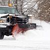 A snow plow is driving down a snow covered road.