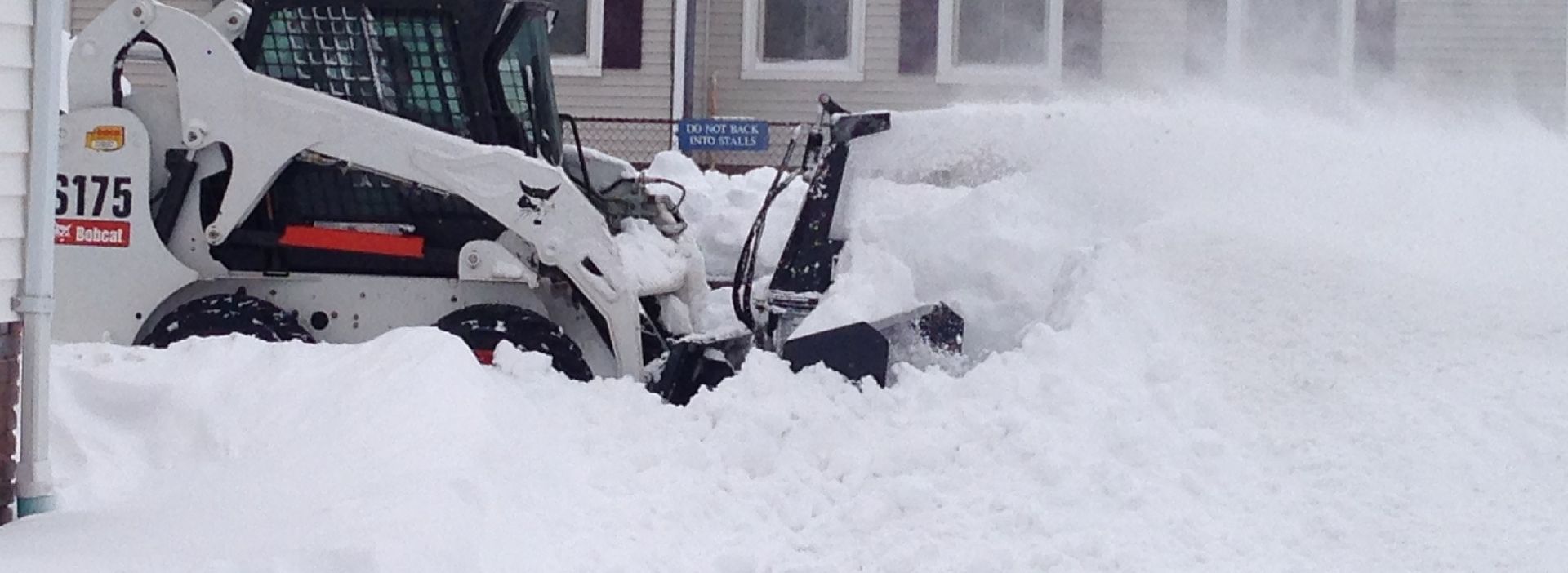 A snow plow is clearing a snowy driveway in front of a house.