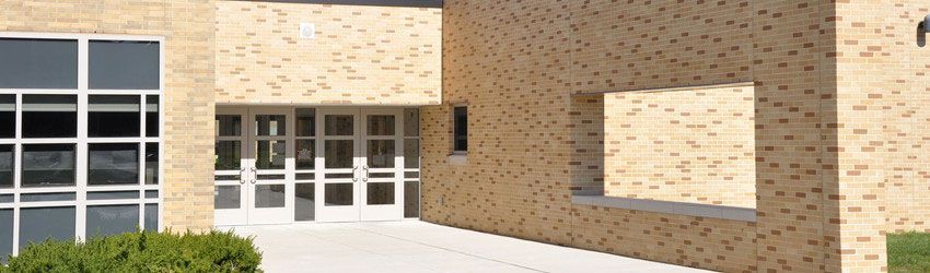 Tan brick school building with courtyard, windows, and white concrete walkway under blue sky