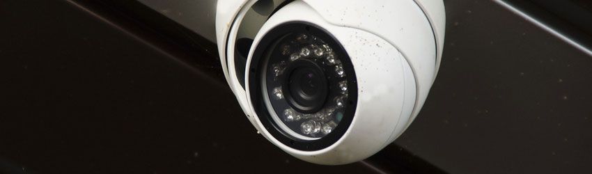 White dome security camera mounted on a dark ceiling panel