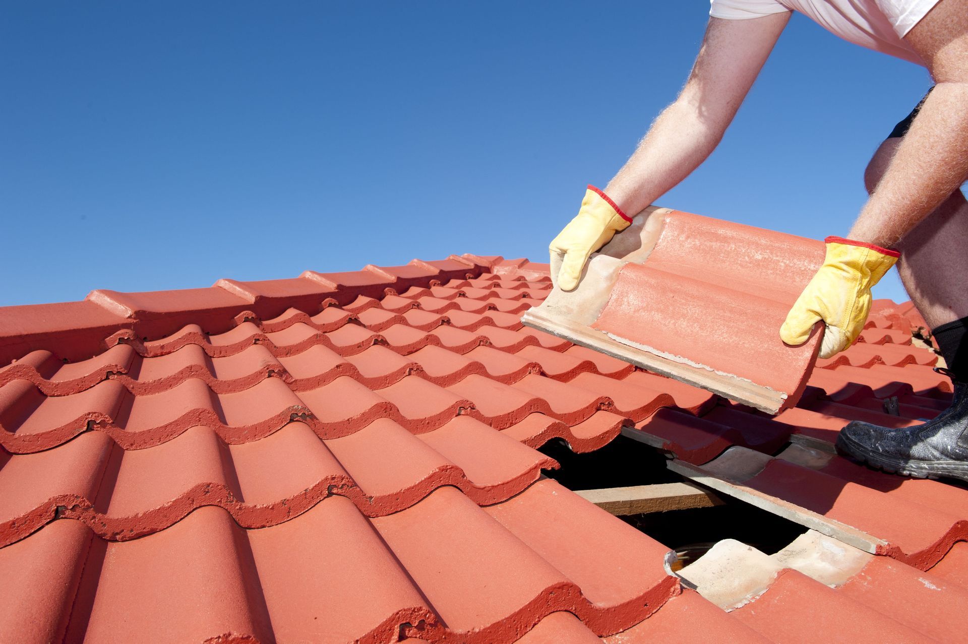 Worker installing red roof tiles on a tiled rooftop under a blue sky
