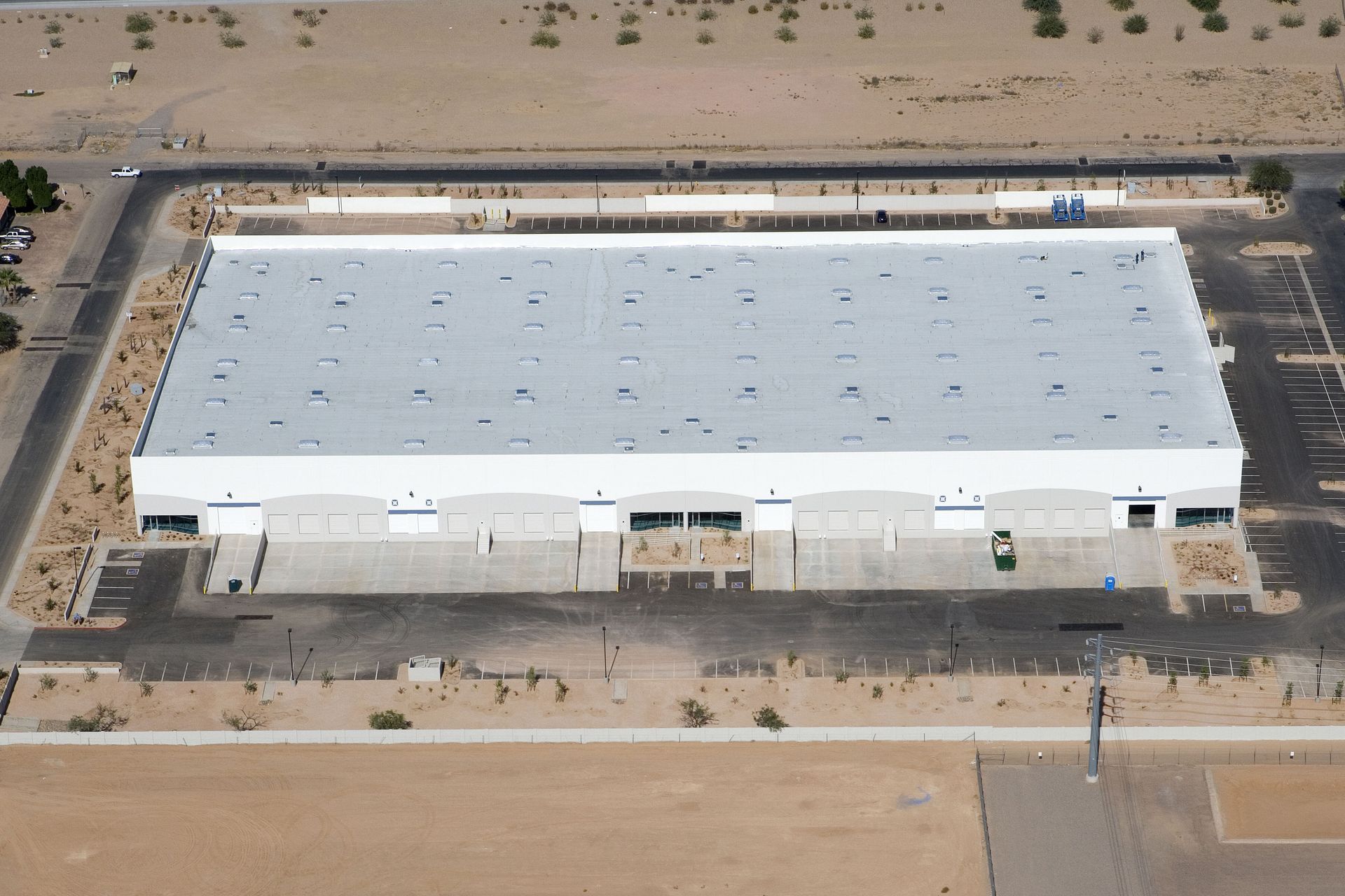 Aerial view of a large white warehouse in a desert lot with surrounding roads and sparse vegetation