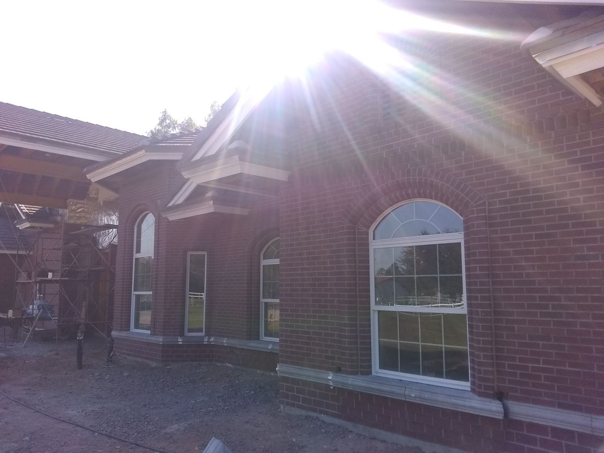 Sunlit brick building with arched window and tiled roof, viewed from the courtyard