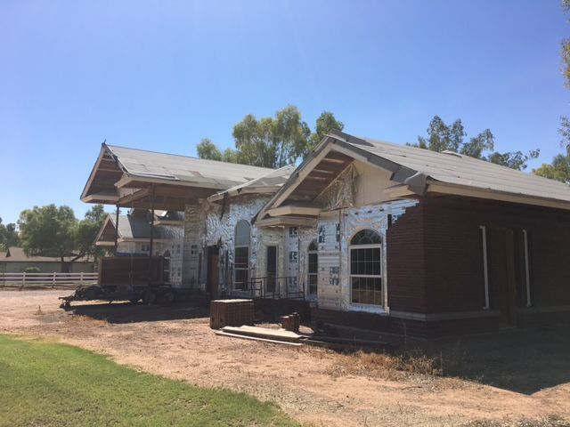 Old white building with red trim and covered porch in a dry, grassy lot under a blue sky