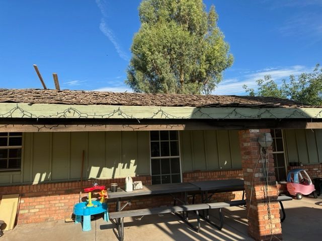 Covered patio with brick columns, bench, and a blue toy table in front of a house under a clear sky