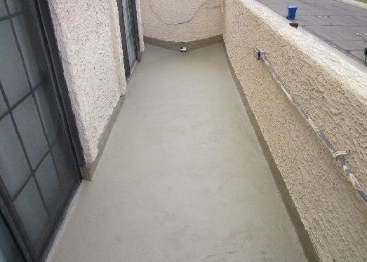 Narrow concrete balcony or walkway with beige walls and a black door on the left.