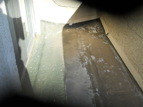 Narrow outdoor walkway with concrete floor, beige wall, and bright sunlight/shadow contrast