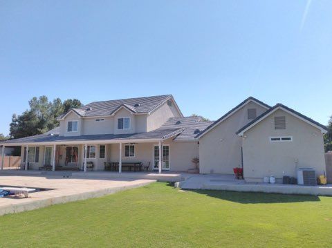 Large beige suburban house with a covered porch, attached garage, and green lawn under a clear blue sky
